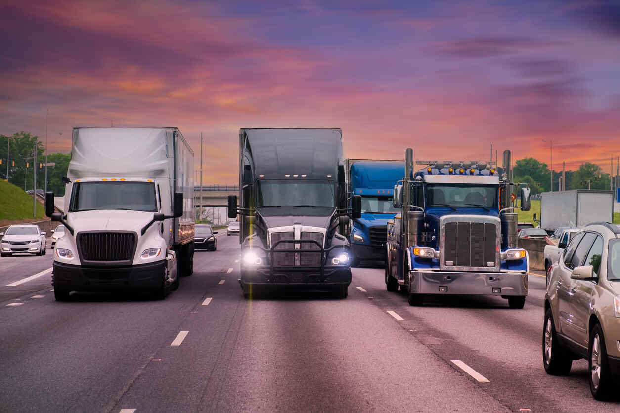 Long-haul trucks in motion on a multi-lane road under a colorful sky, representing the heavy trucking traffic in Houston.